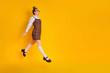 Adorable woman in stylish school uniform jumping joyfully against a vibrant yellow background,...