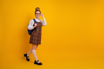 Portrait of a stylish teen girl in school uniform holding a backpack against a yellow background, showcasing back-to-school vibes