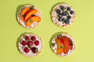 Rice cakes with different types garnish fruits, peaches, blueberries, apricots, raspberries with honey on green background. Healthy colorful food.