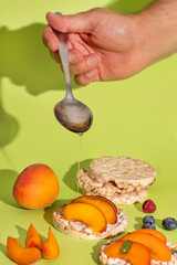 Rice cakes with different types garnish fruits, peaches, blueberries, apricots, raspberries with honey on green background. Healthy colorful food.