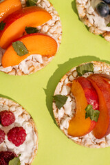 Rice cakes with different types garnish fruits, peaches, blueberries, apricots, raspberries with honey on green background. Healthy colorful food.