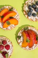 Rice cakes with different types garnish fruits, peaches, blueberries, apricots, raspberries with honey on green background. Healthy colorful food.