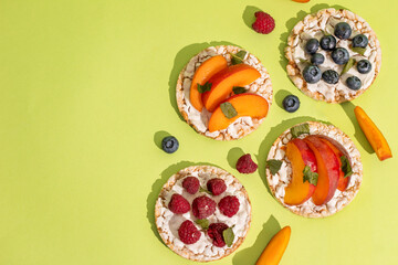 Rice cakes with different types garnish fruits, peaches, blueberries, apricots, raspberries with honey on green background. Healthy colorful food.
