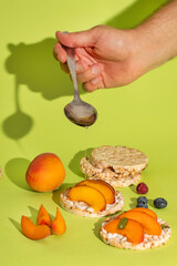 Rice cakes with different types garnish fruits, peaches, blueberries, apricots, raspberries with honey on green background. Healthy colorful food.