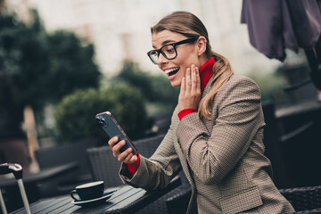 Professional businesswoman excitedly checking smartphone outdoors in autumn city on a modern street...