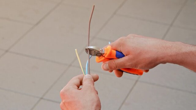 Close up shot of a man cutting two wires in a cable with wire cutters
