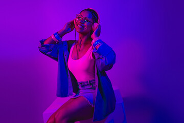 A young woman enjoying music with vibrant neon lighting while showcasing modern casual fashion in...