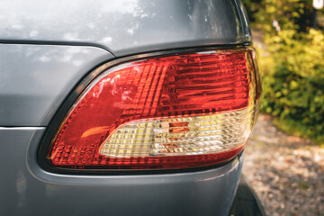 a brake light on a vehicle isolated against a driveway with green plants. red lens for the brake and running lights. transportation and safety background