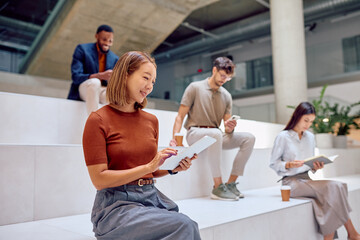 Businesspeople working and relaxing using digital tablet, smartphone and reading book in modern office lobby