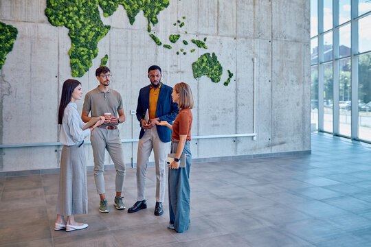 Four managers are discussing global strategy in a modern office with a vertical garden world map made of moss on a concrete wall