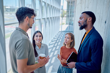 Multi-ethnic business team discussing during a coffee break in a modern office hallway with large...