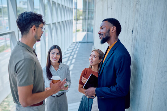 Group of multi-ethnic businesspeople having informal conversation during coffee break in office hallway - Powered by Adobe