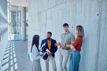 Multi-ethnic businesspeople having an informal meeting while standing in the hallway of a modern office building