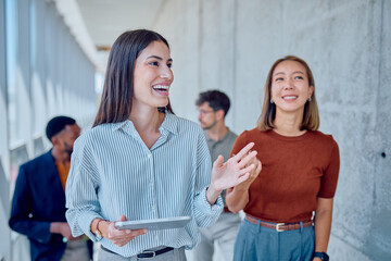 Group of joyful business professionals walking and chatting in a bright office corridor, engaging in collaboration and teamwork