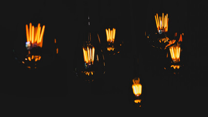 several Edison-style light bulbs with intricate filaments, glowing with a warm, amber light against a dark background. vintage atmospheric aesthetic.