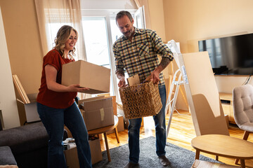 A married couple is moving into their new apartment. They are unpacking boxes together, arranging furniture, and organizing their new living space with teamwork and care.
