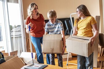 A mother and her kids are unpacking boxes and moving into their new home. They work together to organize their belongings and make the space feel like home. 