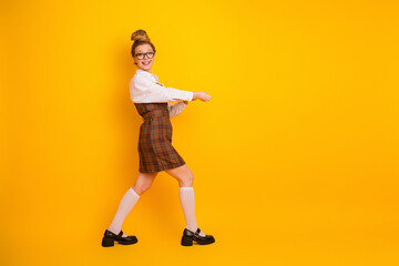 Cheerful young female student posing on vibrant yellow background wearing trendy outfit with a joyful and confident attitude
