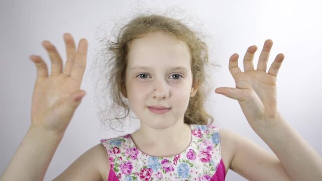 A cute girl smiles, looks at the camera, waves her hands in greeting.