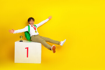 Excited schoolboy celebrating his achievement sitting on a winner's podium with a gold medal on...