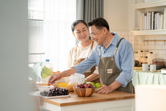 Asian senior couple cooking breakfast in the kitchen. husband helping wife on the morning weekend. Retired people enjoying lifestyle at the preparing counter - Powered by Adobe