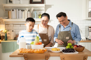 Asian senior couple preparing breakfast with nephew in the kitchen. Happy family spending time on weekend together. Grandparent taking care of grandson. Love and bonding concept