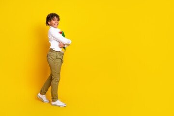 Smiling school boy holding book while posing on a bright yellow background, expressing joy and enthusiasm for education