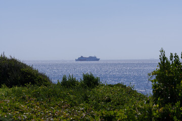 Ferry traversing blue waters, green shoreline visible under bright sunlight