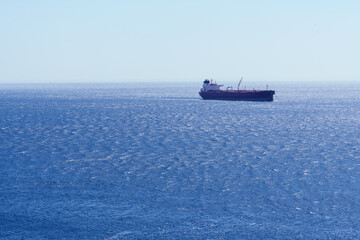Cargo ship navigating calm blue ocean waters on a sunny day, symbolizing global maritime transport and logistics