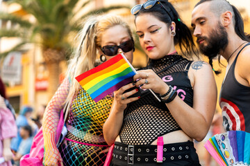 Lgbt friends holding rainbow flag and smartphone at pride parade