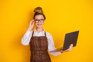 Cheerful young student holding a laptop against a vibrant yellow background, embracing creativity...