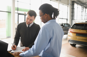 Dealer with male customer signing documents at auto salon. Bearded man in buying new vehicle at car...