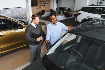 Male car dealer helps customer choose car in car dealership. Man buys new car
