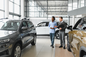 Car Sales Manager Showing Auto To Buyer Standing In Luxury Automobile Dealership Store