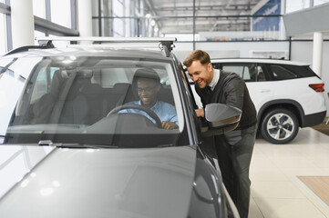 Portrait of male client talking to professional car dealer in dealership.