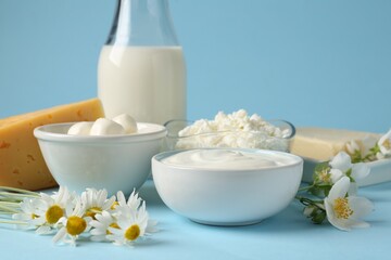 Fresh dairy products and flowers on light blue background, closeup