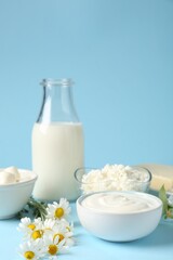 Fresh dairy products and flowers on light blue background, closeup