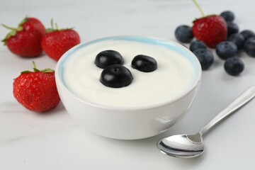 Tasty yoghurt with blueberries and strawberries in bowl on white marble table, closeup