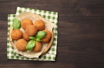 Delicious fried croquette balls with basil on wooden table, top view. Space for text