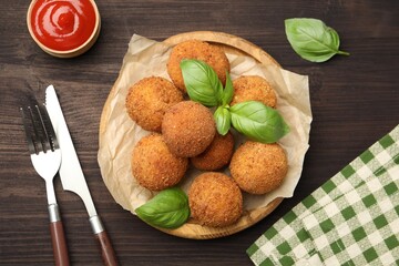 Delicious fried croquette balls with basil, cutlery and ketchup on wooden table, flat lay