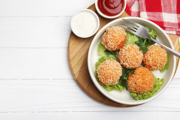 Delicious fried croquette balls with parsley, lettuce and sauces on white wooden table, top view. Space for text