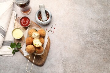 Delicious fried croquette balls with parsley, sauces and spices on grey textured table, flat lay. Space for text