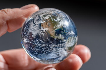 Hand holding a crystal ball with a planet earth inside. Dark background.