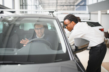 Male car dealer helps customer choose car in car dealership. Man buys new car