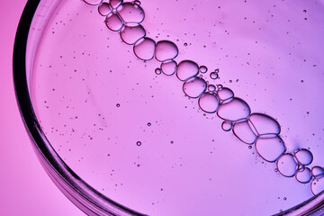 Serum with bubbles in a petri dish on a purple background.