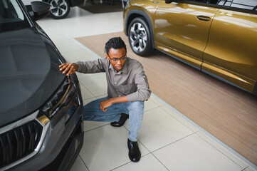Young african american man is choosing a new vehicle in car dealership