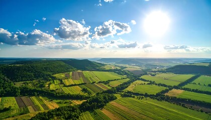 Naklejka premium High-angle view of rolling hills, fields, and forests under a vibrant blue sky