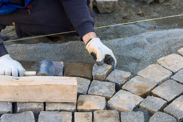 Skilled worker carefully positions stone bricks for pathway, ensuring they fit securely evenly on...