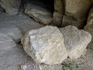 A large rock sits in the dirt, surrounded by smaller rocks. The scene is desolate and barren, with...