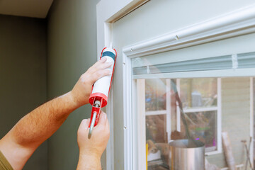 Contractor is using caulk gun to seal gaps around window frame during home improvement task.